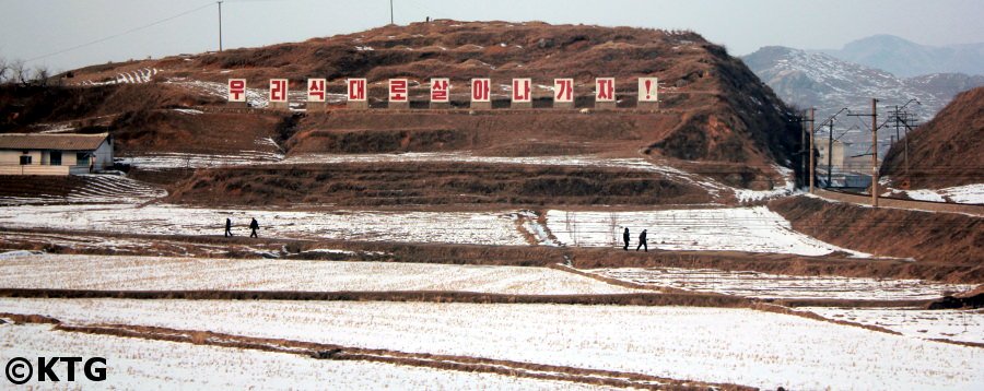 Campagne nord-coréenne en hiver avec un slogan géant. Visitez la RPDC avec KTG Tours